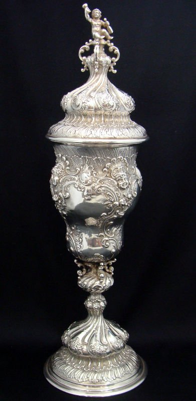 800 German Silver Covered Cup: 800 German silver cup with a figure on lid as its finial. Features detailed scroll work and flower design throughout. This is a very ornate piece. Weighs 18toz. Measures 14" tall. For Domestic or Inte