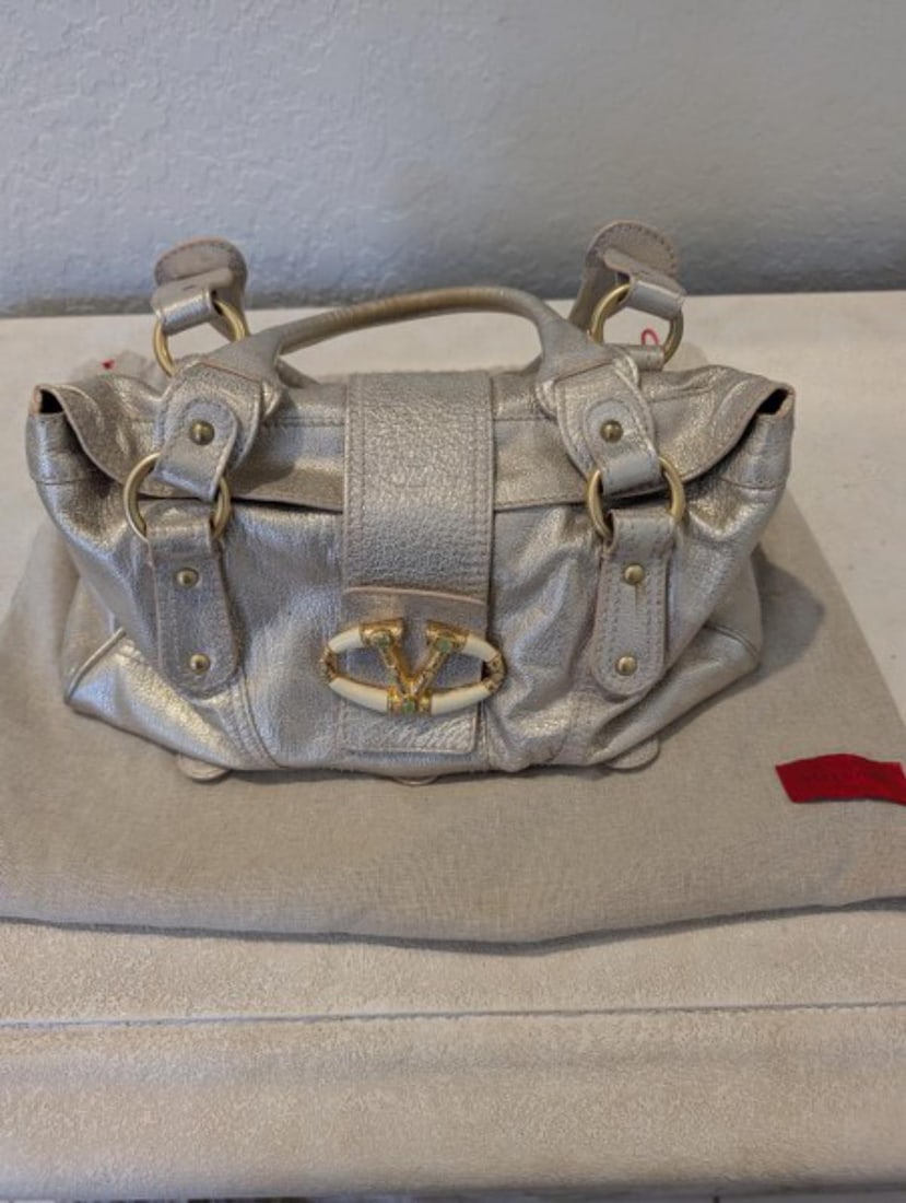 Authentic Valentino Garavani Metallic Leather Handbag with Dust Bag: Authentic Valentino Garavani metallic leather handbag featuring the iconic Valentino 'V' hardware, gold-tone accents, dual leather handles, and a soft structured silhouette. Finished in an elegant met