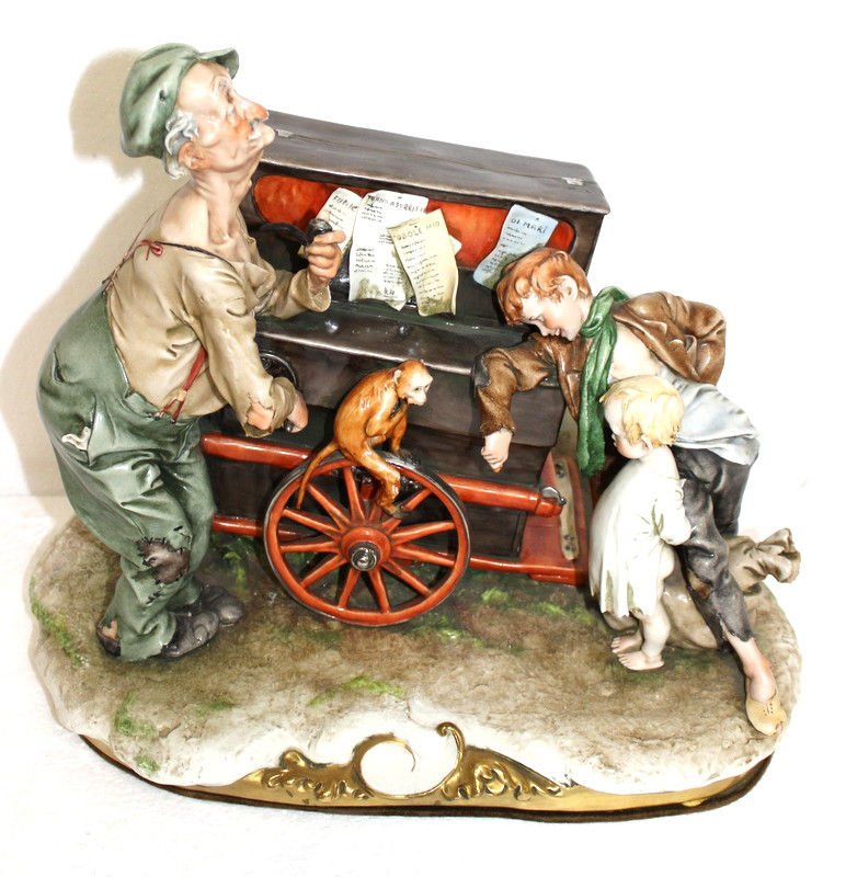 Guiseppe Armani Capodimonte Organ Grinder: Guiseppe Armani Capodimonte Organ Grinder featuring an old man with children and an old organ grinder organ with music box inside that plays music. Figurine measures 8 1/2" x 9" x 5". Condition - musi