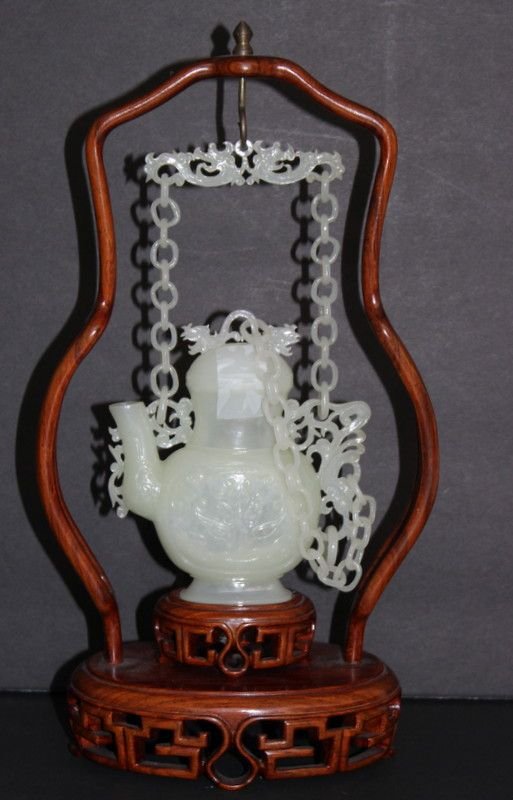 Chinese Jade Hanging Covered Vase: Fine Chinese Jade Hanging Covered Vase. Enclosed by a wooden open work holder with lose rings, on a wooden stand with hanging frame. Jade measures - 7" high x 4" wide. Total measures - 11 1/2" high x 