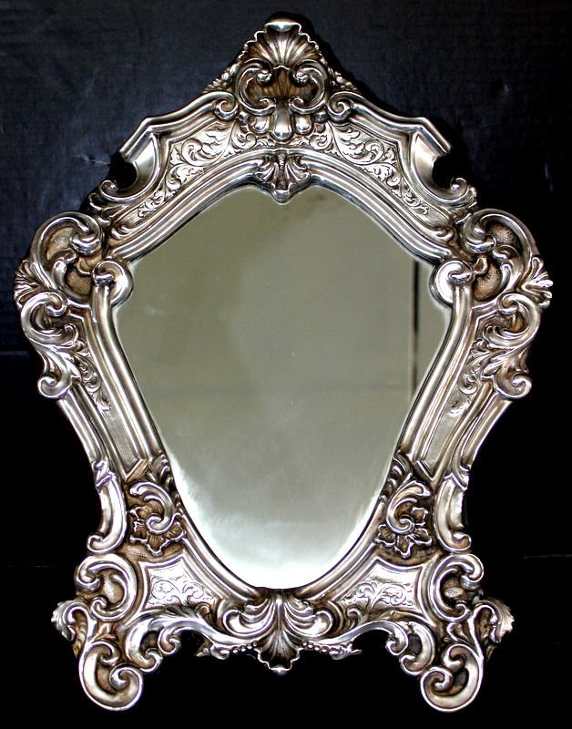 Sterling Silver Vanity Mirror: Sterling Silver Vanity Mirror with ornate scroll design. Measures - 17 1/2" high x 13" wide.