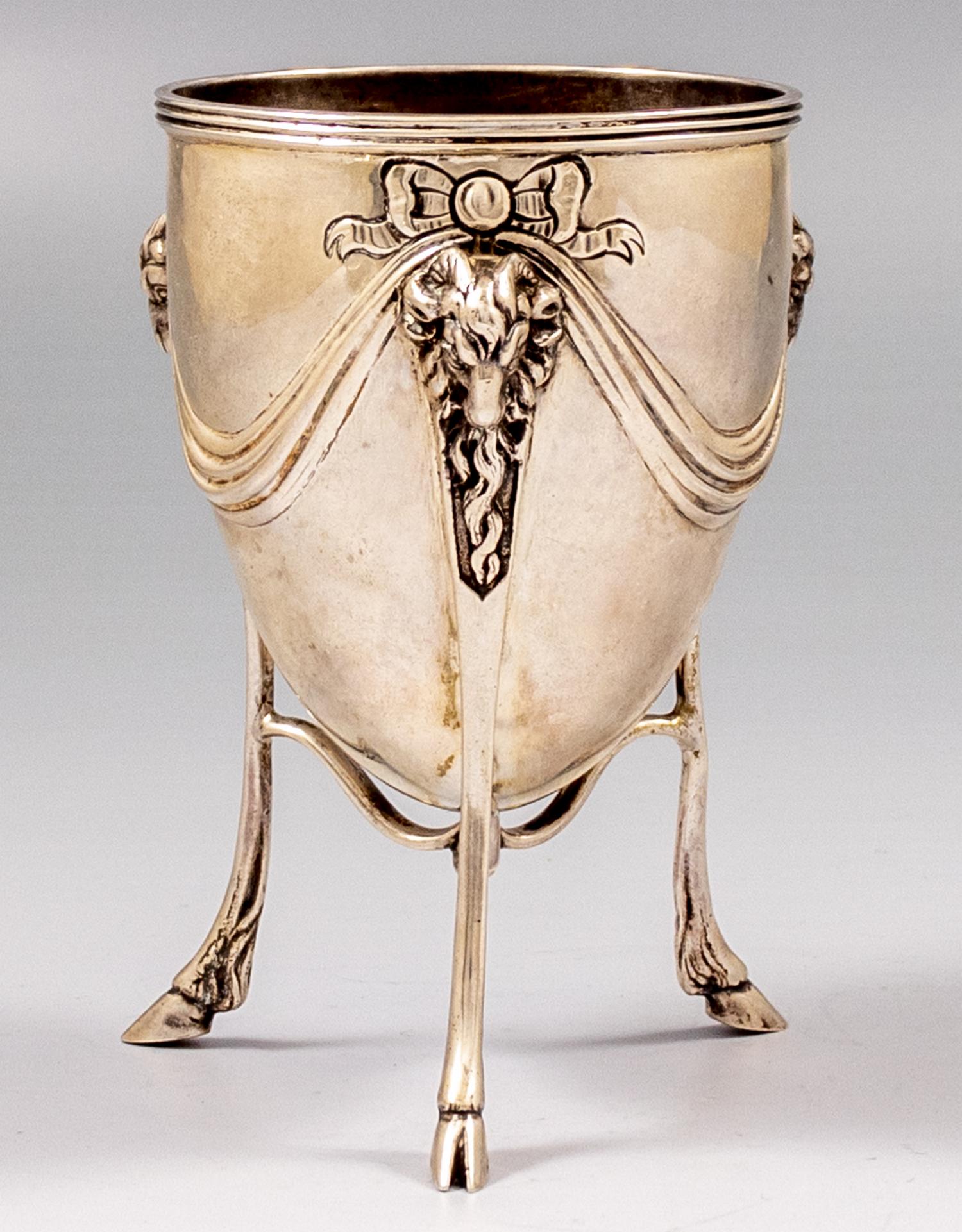 English Silver Goblet: English silver goblet by Charles Stuart Harris, London, 1899. Decorated with ram heads. Stands on 3 legs. Height: 12.5 cm. Weight: 199 grams. Marked. A minute dent.
