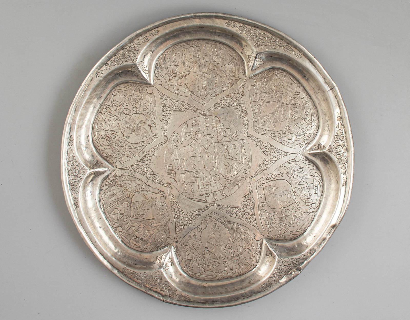 Persian Silver Serving Items: Persian silver tray. Engraved with figures in various scenes and floral decorations. Diameter: 27.5 cm. Weight: 502 grams. Hallmarked.