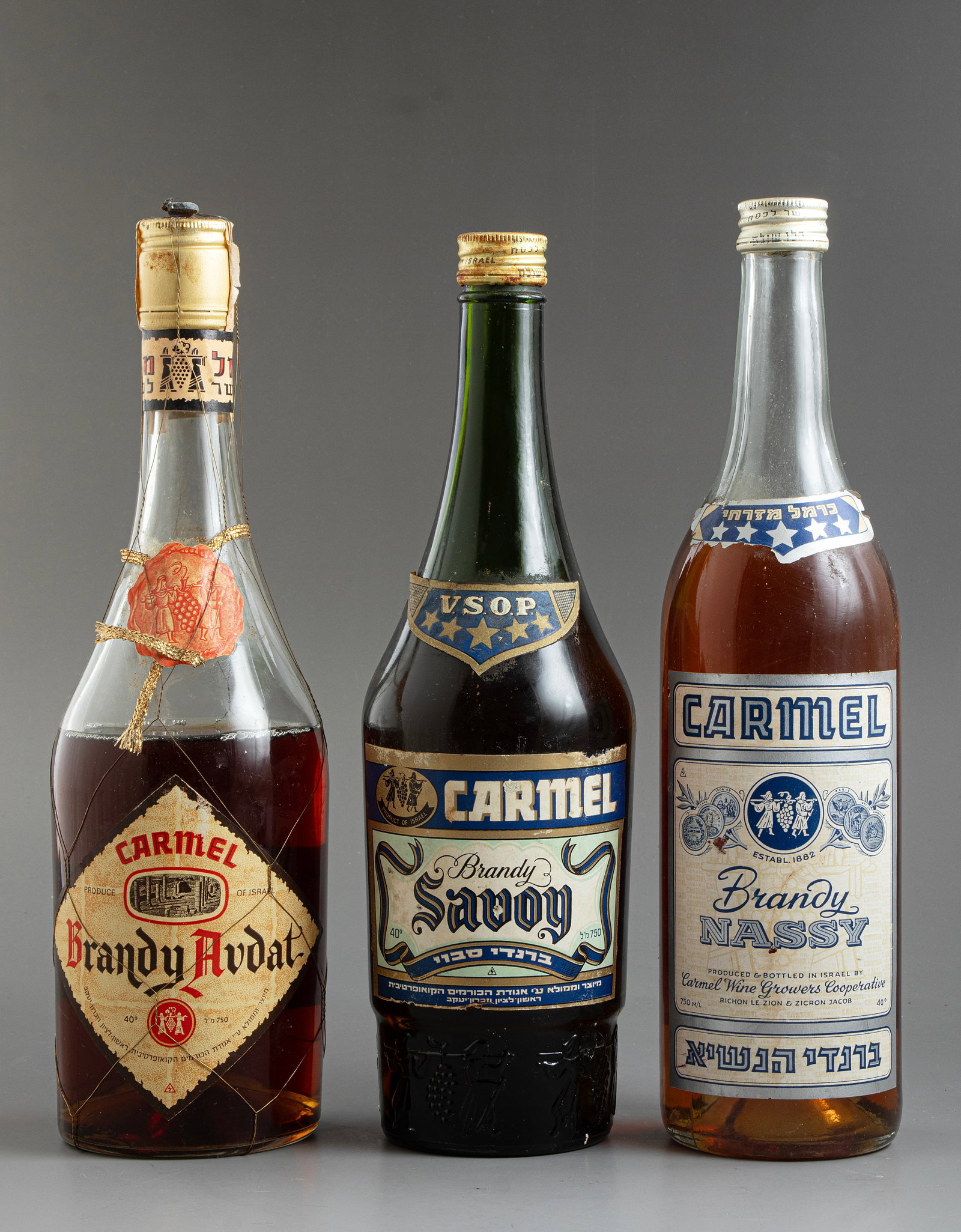 Israeli Brandy Bottles: Lot of 3 vintage Israeli brandy bottles by Carmel Mizrahi, including “President,” “Savoy,” and “Avdat.” Sealed, never opened. Various conditions, due to its age