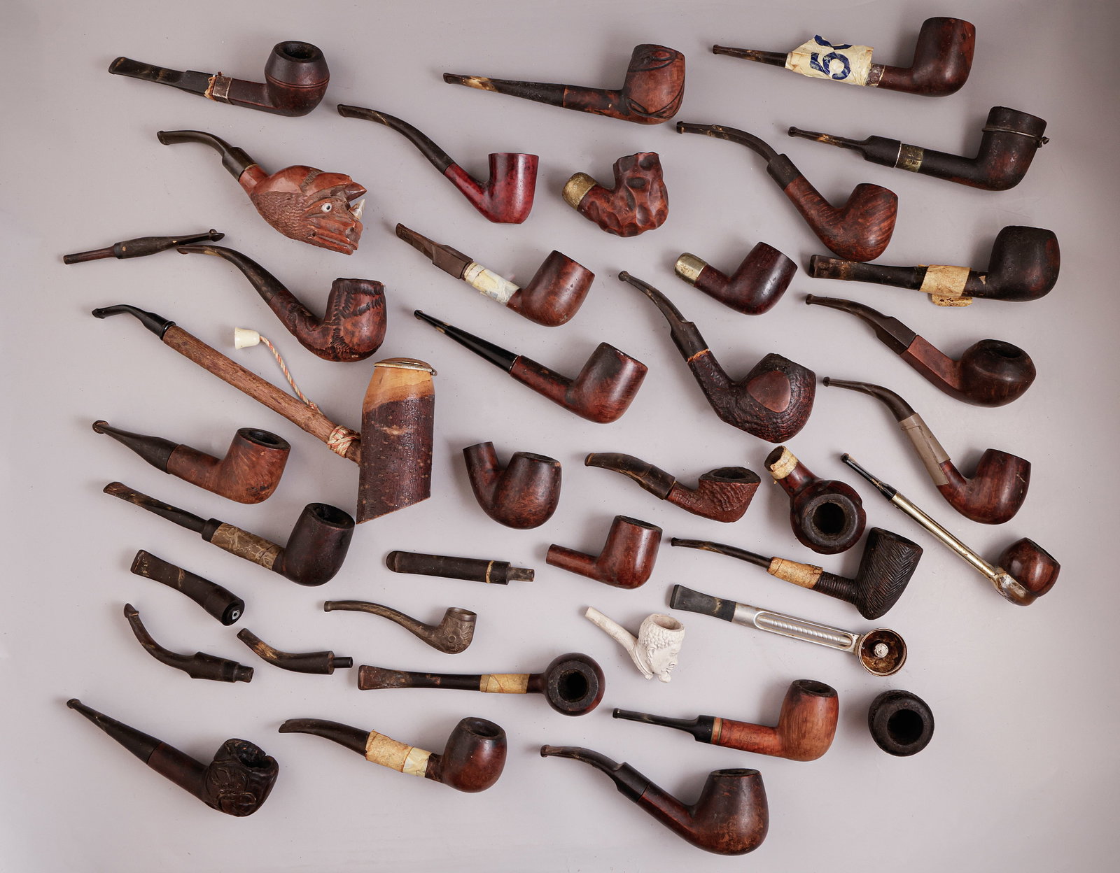 Smoking Pipes: Lot comprising more than 25 smoking pipes, made of various materials including wood, metal, and meerschaum. Some carved as faces and some mounted with silver. Length: 10–24.5 cm. Pipe parts