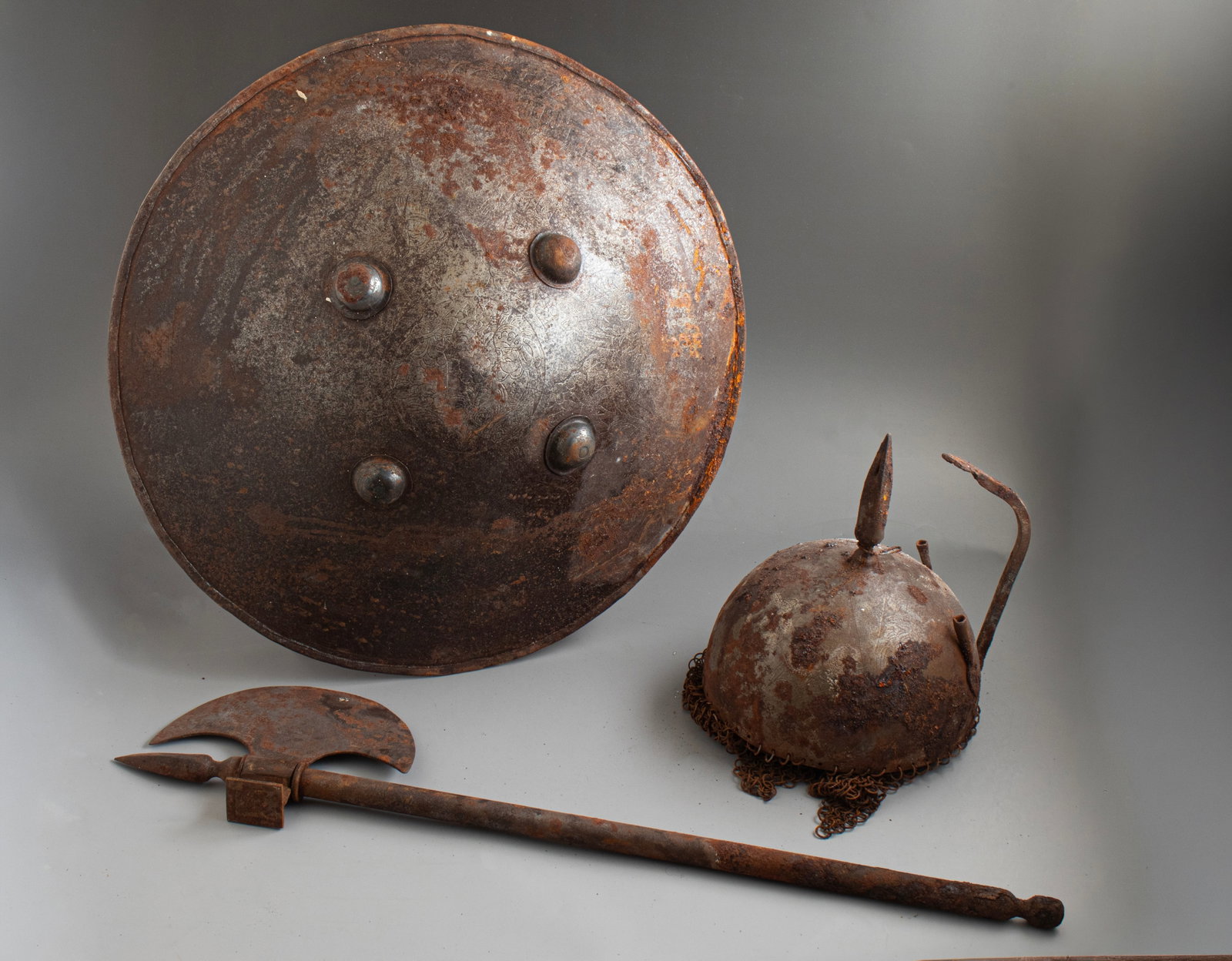 Persian Shield, Helmet & Axe (Kulah khud): Set of Persian iron shield, helmet and axe (Kulah khud). Etched decoration with figures and floral motifs. Height of the helmet: 25 cm. Sheild diameter: 48 cm. Axe length: 66.5 cm. Wear and rust.