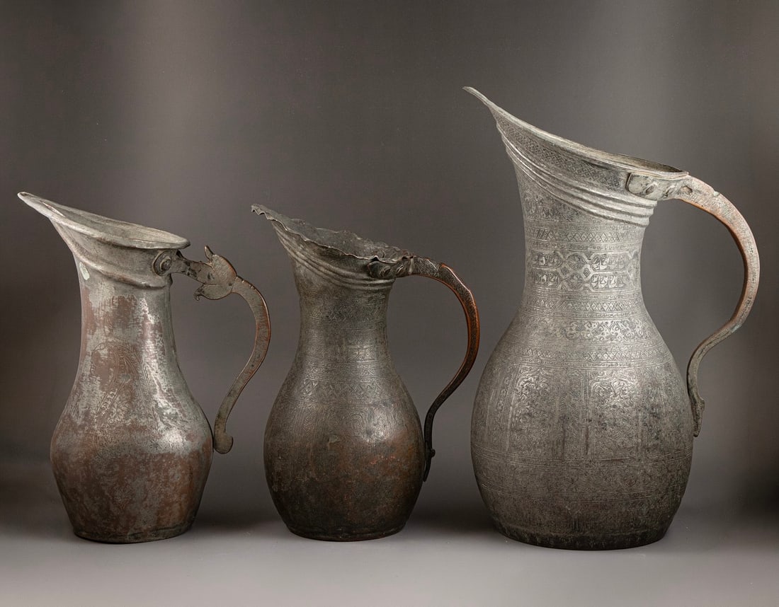 Persian Pitchers: Lot of 3 Persian pitchers, made of tinned copper. Decorated with floral, geometric and calligraphic motifs. Height: 33–44.5 cm. Minor dents, slight wear to the plating.