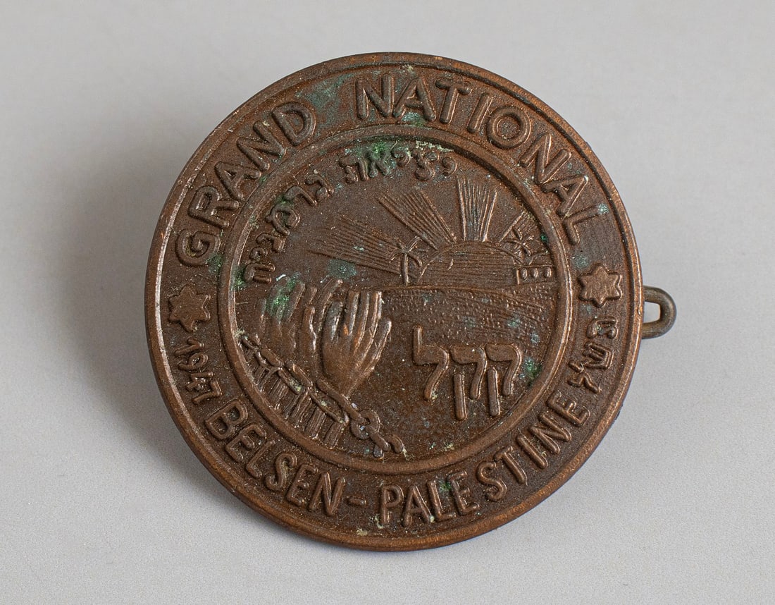 She'erit Hapleita JNF Lapel Pin: She'erit Hapleita copper lapel pin by the JNF, given to refugees in the Bergen Belsen DP camp. Depicts the hands of a prisoner breaking his handcuffs. Also bears the writings: BELSEN-PALESTINE and