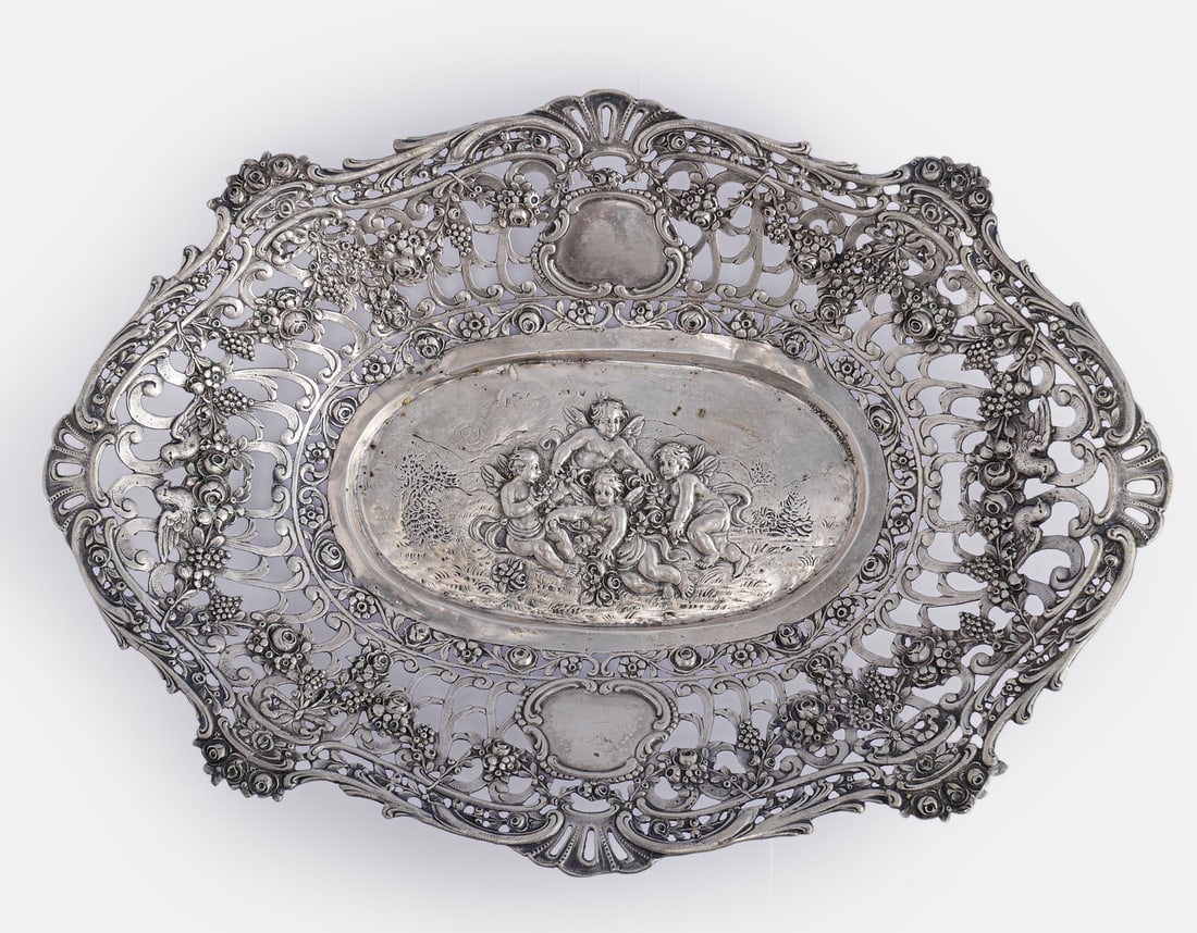 German Silver Bowl: Fine German silver bowl, early 20th century. Centered with a relief depicting angels, the rim decorated with openwork and relief decoration of fruits, flowers, and birds. Length: 29.5 cm. Weight: 239