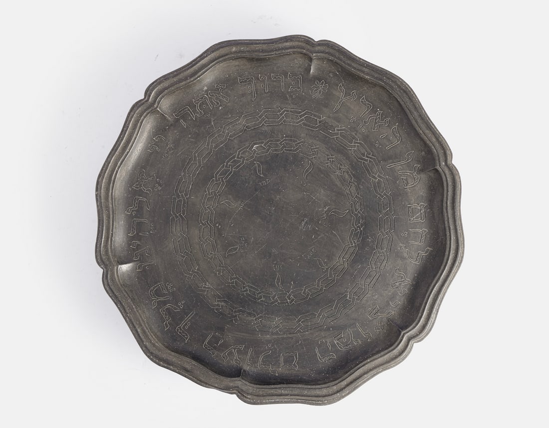 Pewter Shabbath Tray: Pewter Shabbath tray, Central/Eastern Europe, 19th century. Decorated with engraved floral motifs and a Hebrew inscription. Stands on three legs. Height: 6 cm. Diameter: 34 cm. Minor flaws (dents).