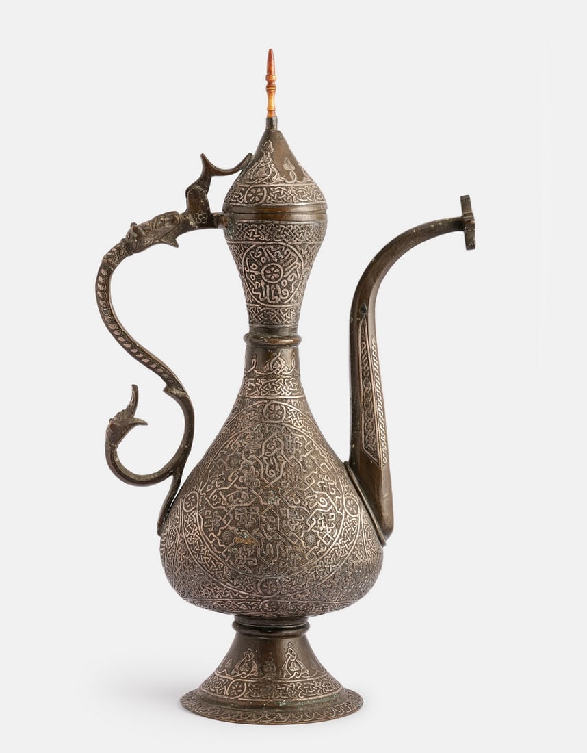 Damascene Brass Ewer: Fine Islamic brass ewer, inlaid with silver (Damascene). Decorated with arabesques, floral and calligraphic motifs. Height: 37.5 cm.