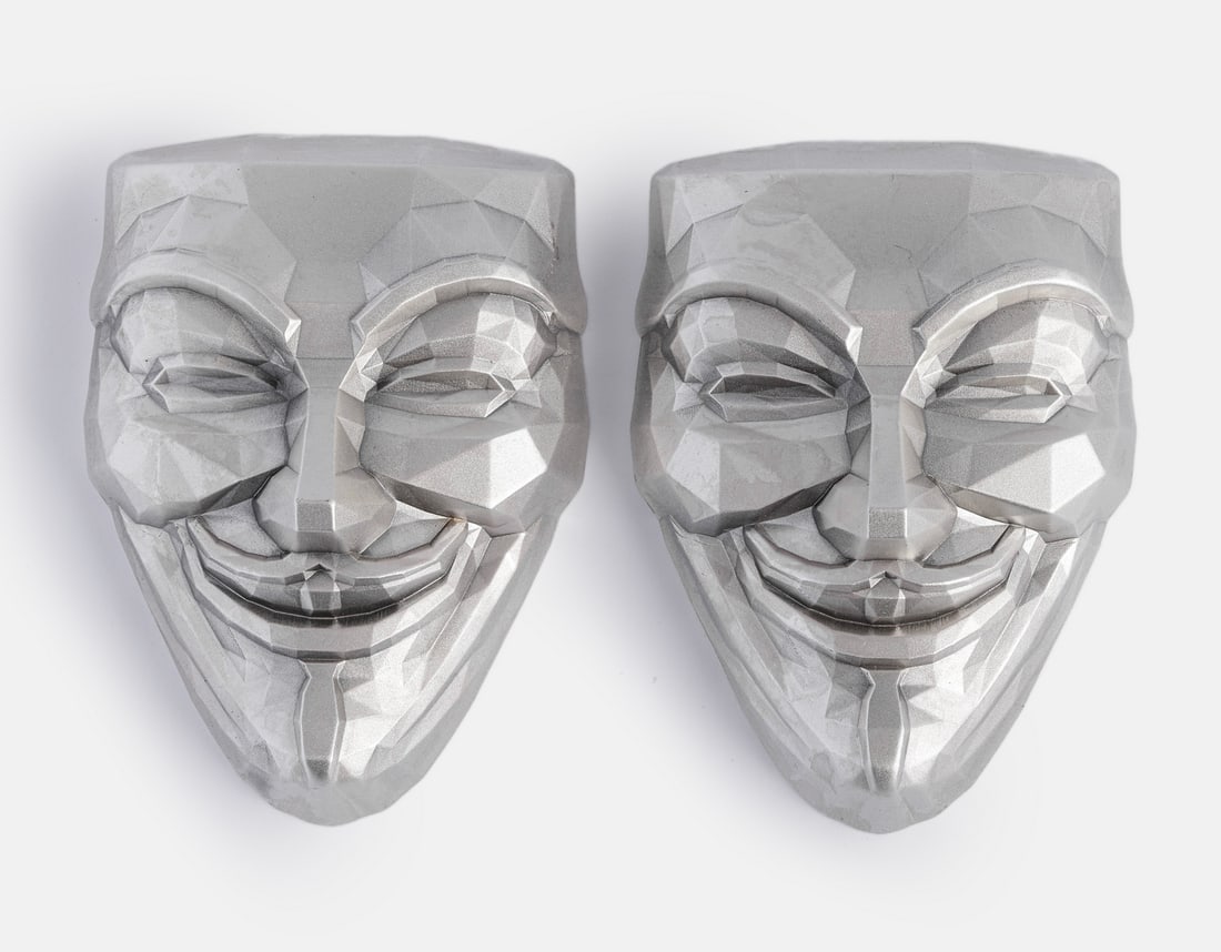 Silver “V for Vendetta” Masks: Lot of two miniature 999 silver “V for Vendetta” masks, South Korea, each weighing 2 Oz. Housed in fitted plastic cases. Total weight: 125 grams. Hallmarked.