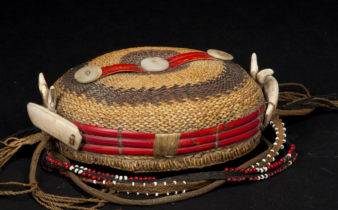 A Bontoc hat: Luzon, Philippines; D: 8" The hat of classical form; the cap itself of plaited basketry fiber in yellow and brown with highlights in red, the top with attached buttons. The sides with boar's tusks and
