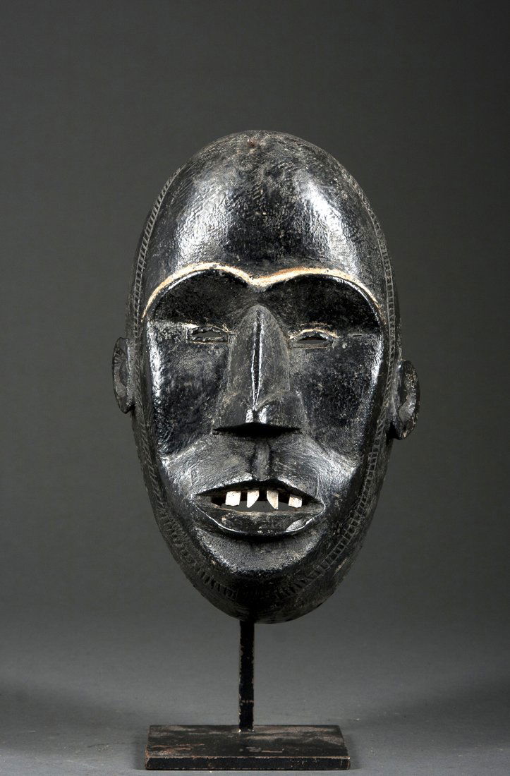 A Dan/Mano mask: Dan/Mano, Liberia; H: 10 1/2 inchesThe mask with High rounded forehead and high browline, the cheeks angular and the nose pointed, the lips open showing metal teeth, the chin well carved. On a custom
