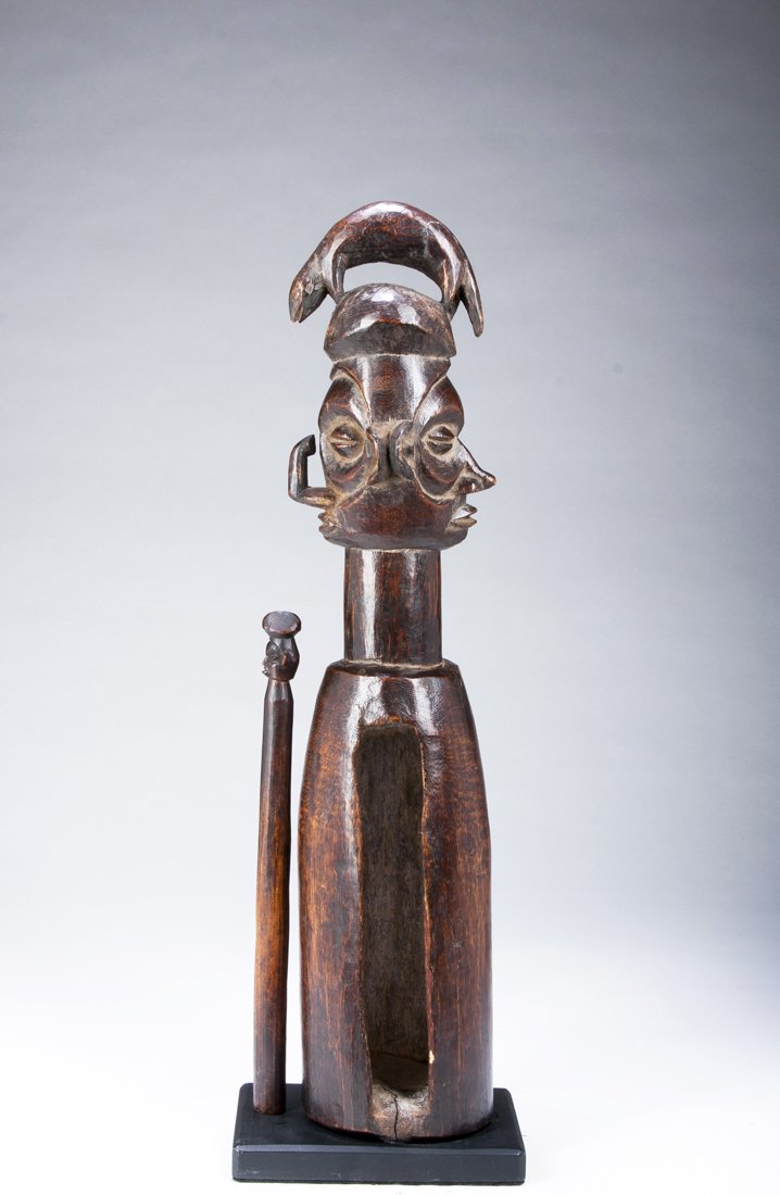 A fine Yaka Janus slit drum: Yaka, D. R. Congo; Height: 19 3/4" The drum of unusual form with a quadruped, possibly a lizard, atop the Janus head; the faces well carved, the noses indicating a male/female dichotomy. Fine patina. 