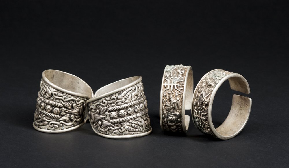 Two Pair of Miao Bracelets: Two Pair of Miao Bracelets. The first a set of wide cuffs with raised designs depicting animals and a central band of smiling faces. The second narrower and with raised animal motifs. Silver content o