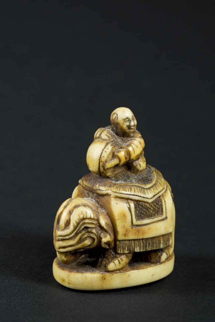 Mammoth Ivory Katabori Netsuke: Mammoth Ivory Katabori Ivory Netsuke of a young boy playing a drum while seated on an elephant, nicely carved with dark yellow patina in spots due to age, 1 3/8" tall. Mammoth ivory fluoresces to purp