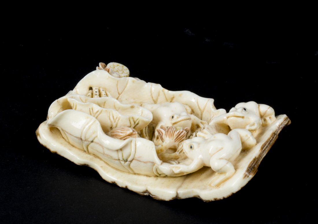 Netsuke of Three Frogs: Netsuke of Three Frogs, carved from mammoth ivory in the 20th century showing 3 frogs amoung water flowers. Brown fossilized crust of the ivory is on the underside as is the carved artists signature. 