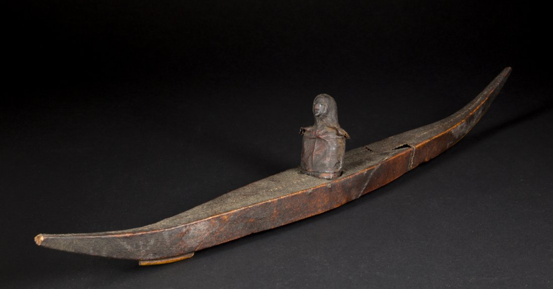 Inuit Miniature Kayak and Figure: Inuit Miniature Kayak and Figure: a 23" L kayak made of stitched hide on a wooden frame with a hide and wood carved figure of a man inserted in the center, probably had arms and paddle at one time, so