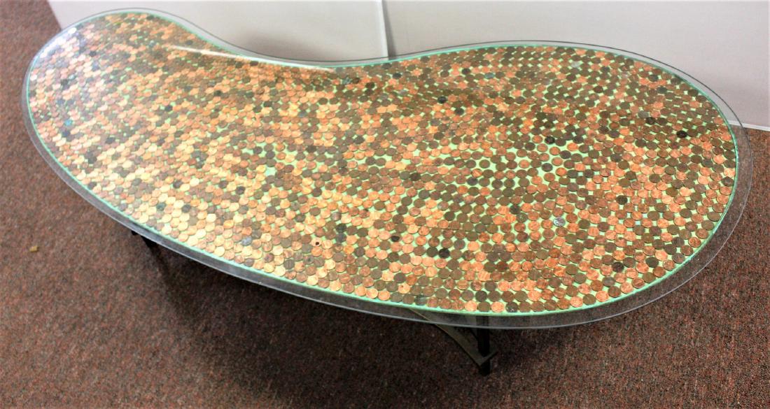 Mid Century Glass Top Coffee Table: Kidney shaped coffee table. Glass top. Metal legs. U.S. Penny inlaid top; 15.5in.H. x 60in.W. x 25in.D.