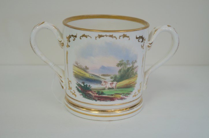 Hand Painted Porcelain Trophy Mug: Two(2) handled porcelain trophy mug. Painted scenic decoration. A pastoral scene. Gilt inscription reads, Presented to Timothy Malkin by his Dearest Friend EH 1870; 5in. H. x 8.5in. W.