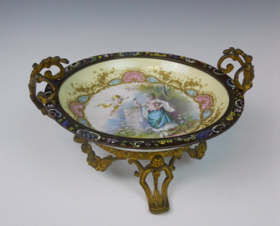 French Ormolu Mounted Porcelain Compote, Sevres: Porcelain bowl with hand painted image of a female figure and putti in a garden setting with embossed gilt accents and champleve rim. Set in decorative ormolu mount. Sevres maker mark at bottom - lett