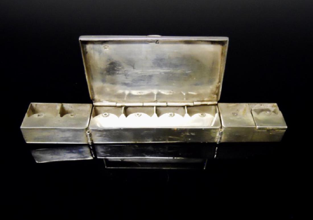 Continental Silver Traveling Chanukah Lamp: Box form with hinged candle bases. Cover with hand-chased decoration depicts man lighting a traditional menorah. Interior with eight hinged candle bases fold into a menorah. The lid carries a star hal