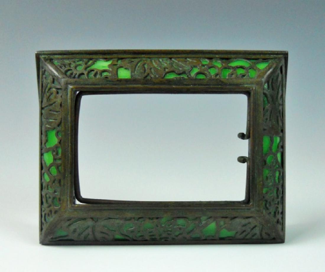 Bronze and Glass Picture Frame, TIFFANY STUDIOS: Antique bronze and stained glass desk top picture frame, signed "TIFFANY STUDIOS NEW YORK 930". Frame with bronze overlay with green glass backing. Measures: 3.5" H x 4.5" W