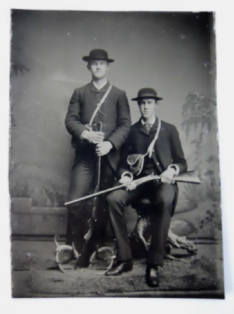19th C. Tintype Photograph, Two Hunters Armed: Antique 1/6th plate tintype photograph of two hunters with rifles, with antlers at feet. Image is under glass with gold foil frame, set in tooled leather case with velvet keeper. Measures: 3.75" H x 3