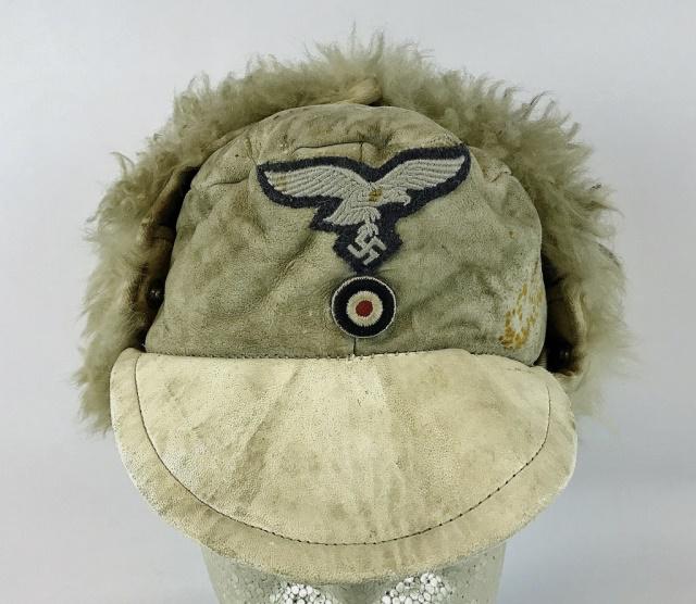 WW2 German Luftwaffe Winter Field Cap: World War Two German Luftwaffe Winter field cap. White leather construction with wool earflaps. Hand applied two piece insignia with eagle over cockade. Interior lined in wool. Good field worn conditi