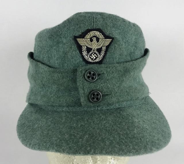 WW2 German Schutzpolizei EM / NCO Field Cap: World War Two German Schutzpolizei M1943 field cap. Blue-green wool construction, earflaps secured by two bakelite buttons. Hand applied one piece BeVo woven wreathed eagle insignia. Interior cloth li