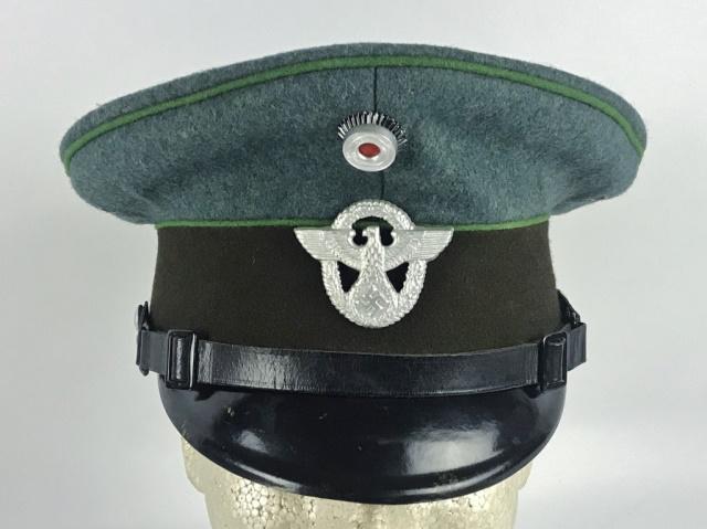WW2 German Schutzpolizei EM / NCO Visor Cap: World War Two German Schutzpolizei EM / NCO visor cap. Grey - blue wool construction with four metal ventilation grommets, brown band, green piping, two buckle adjustable leather chinstrap and lacquer