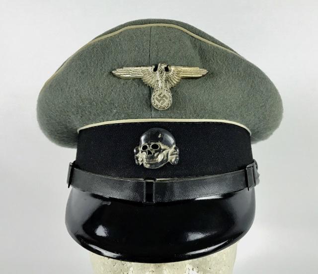 WW2 German SS EM / NCO Visor Cap: World War Two German SS EM / NCO visor cap. Constructed of grey wool with black band and white piping, black leather chinstrap with black lacquered vulcanfibre visor. Cap has die struck silver washed 