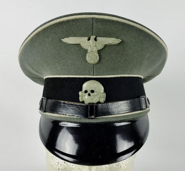 WW2 German SS EM / NCO Visor Cap: World War Two German SS EM / NCO Visor Cap. Constructed of grey woven wool with black band and white piping, black leather chinstrap with black lacquered vulcanfibre visor. Cap has die struck metal SS