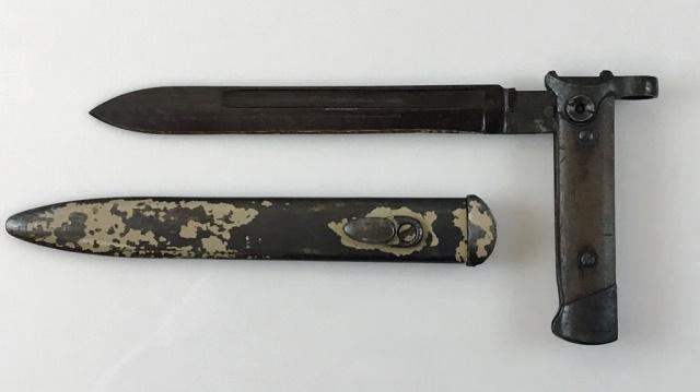 WW2 Italian 38A SMG Folding Bayonet, Beretta: World War Two Italian 38A SMG Folding Bayonet. Wood grip with blued pommel and guard. Blade hinged with button release locking and folding in place. Steel scabbard with stud, remnants of desert ordina