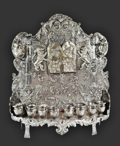 Antique Silver Hanukkah Menorah: Antique Silver Israeli Hanukkah Menorah. Traditional candelabrum featuring an upright back plate with profuse floral and foliate repousse and hand chased embellishment. Eight decorated urns rest on pe