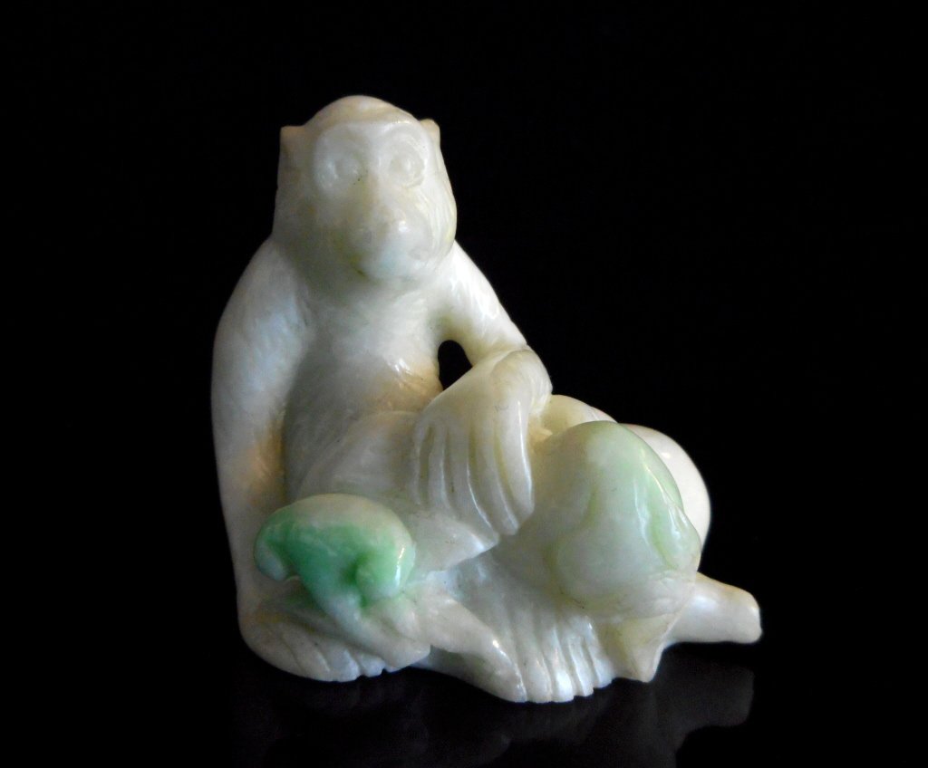 Jade Monkey With Peaches: White jade rendering of a seated monkey holding a cluster of peaches. Smooth polished surface with green suffusion. 2"H