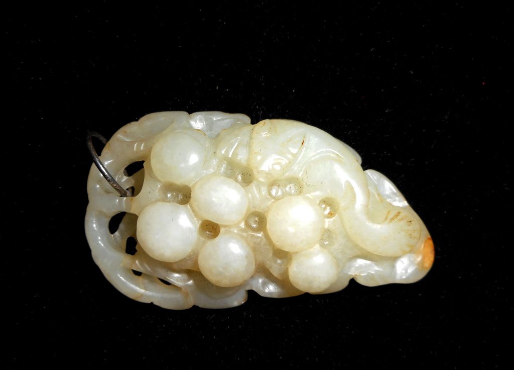 Jade Grape Pendant: White jade openwork pendant depicts a grape bunch carved in relief resting on a leaf bed surmounted by a small woodland creature with incised details. Smooth polished finish with areas of slight yello