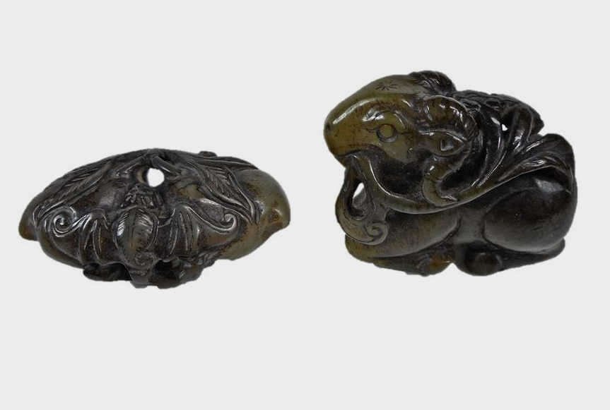 Two Jade Figures Peach and Ram: Two dark greenish-grey openwork jade carvings, each having smooth polished surfaces with incised details, darker areas of brown or black suffusion and veining. Soil is visualized in crevices of both c