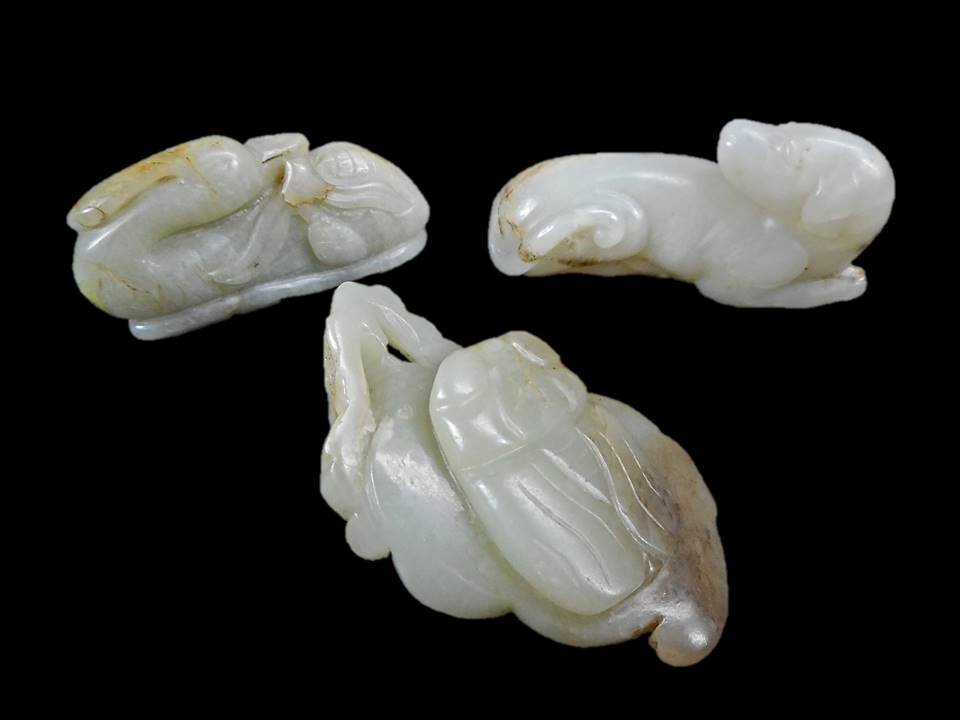 Three Jade Figures: Collection of carved jade figures. One in the form of a recumbent dog with his head turned backward in white jade, having a smooth polished surface with tan, russet and white suffusion and veining. 2.