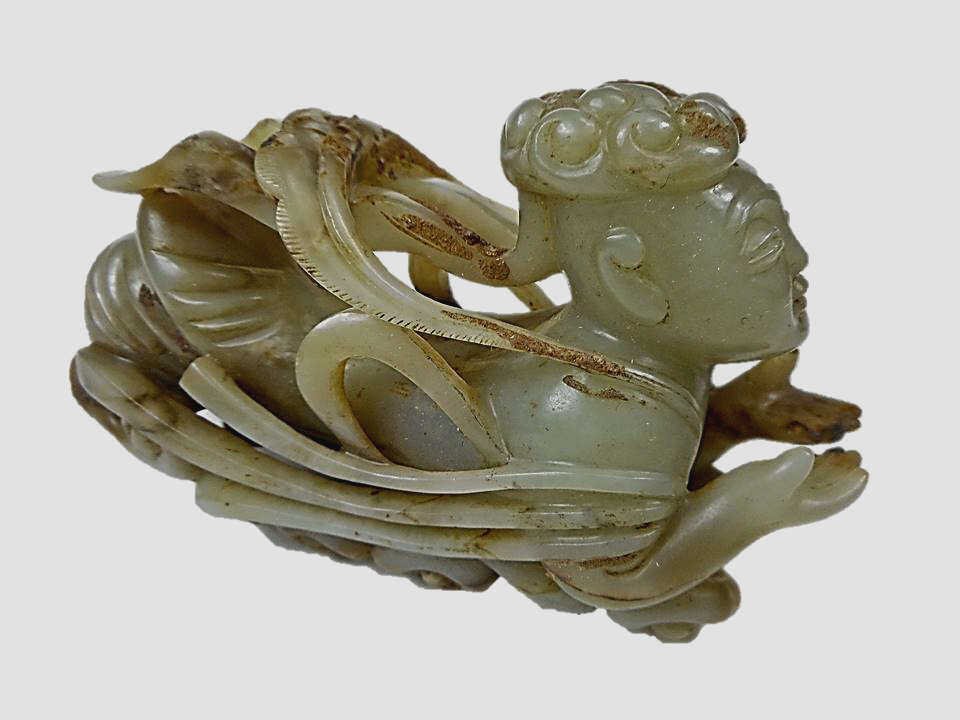 Jade Celestial Deity: Grey-green jade rendering of a celestial deity with openwork swirling cloud pattern design and incised details carved in relief. Smooth surface with tan and dark brown suffusion. Exhibits corrosion an