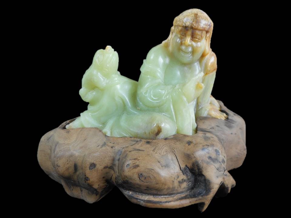 Jade Man and Toad Figure: Green jade carving of a man with a three-footed toad. Smooth surface with incised details, tan and brown suffusion at head, left hand and back. Presented on wooden stand.