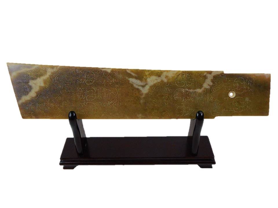 Jade Ceremonial Blade: Bearing delicately incised figures in alternating pattern. Brown, black and russet suffusion observed with scattered corrosion. Includes stand. 16"L