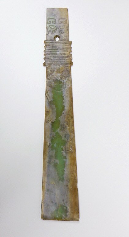 Jade Gui, Western Zhou Dynasty (1046-771 BC): Green jade Gui having a smooth polished surface with tan colored suffusion. Blade and handle feature anthropomorphic mask, dragon and cloud designs carved in bas-relief. There is a 0.5" area of loss t