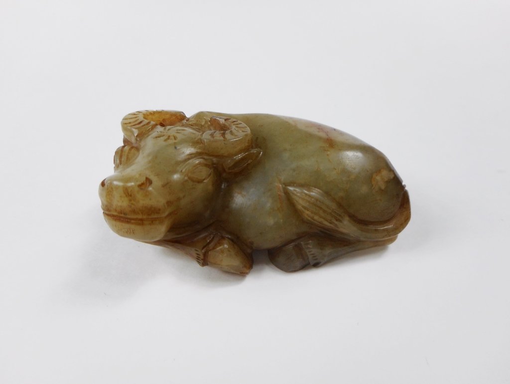 Jade Ox: Green jade rendering of a recumbent ox. Smooth surface with russet and brown suffusion at tail and bottom and slight erosion. Incised details. 2.5"L