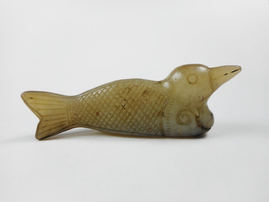 Jade Fish and Bird: Grey-white jade carving of a two-headed mythological creature having the body and head of a fish as well as the head of a bird. Dark brown and black suffusion near bottom. Finely incised details. 3.25