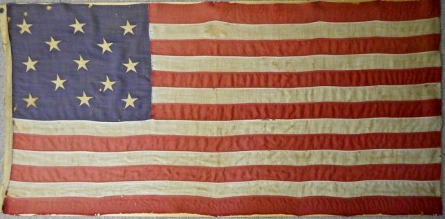 19th C.Thirteen Star American Flag: 13-Star American flag in 3-2-3 configuration zig zag sitch star application. Flag is tacked to board under glass in wood frame. Age tone with scattered areas of loss on blue and white backgrounds. Cir