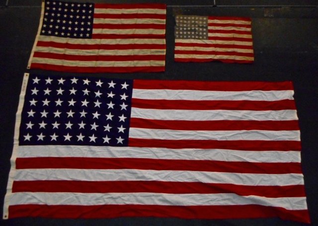 Three WWII United States Flags: Three Forty Eight Star WWII era flags: two have sewn stars and stripes with brass grommets. The largest flag bears maker mark, "Bulldog Bunting". Smallest flag is screen printed. Sizes range from 33"H