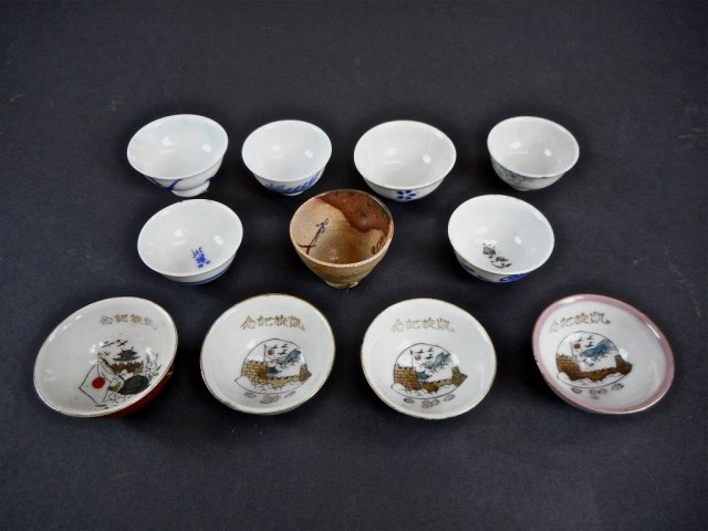 Collection of Japanese WWII Sake Cups: Four cups featuring military scenes with gilt accents, signed on bottom. Six are blue and white with varied designs, one is earth tone with crackle glaze. Wear consistent with age and use