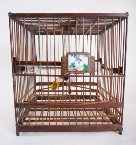 Antique Chinese Birdcage: Having two hand decorated porcelain feeders, three attachments with chinoiserie imagery, a jade ring is suspended from a silk cord. Decorative metal plate at top features embossed rams in pastoral sce